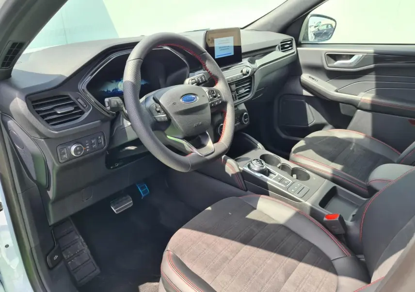 Intérieur avant droit du Ford Kuga blanc Glacier 2022, sièges sport noirs avec surpiqûres rouges et volant ST-Line.