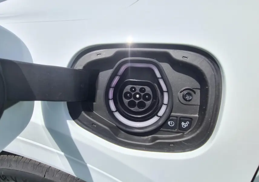 Prise de recharge hybride côté gauche d'un Ford Kuga blanc glacier, avec port de charge ouvert et boutons de commande visibles.