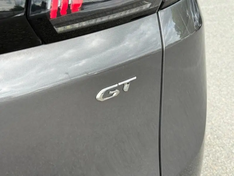 Détail du logo GT sur l'arrière droit d'un Peugeot 3008 gris Platinium sous lumière naturelle.