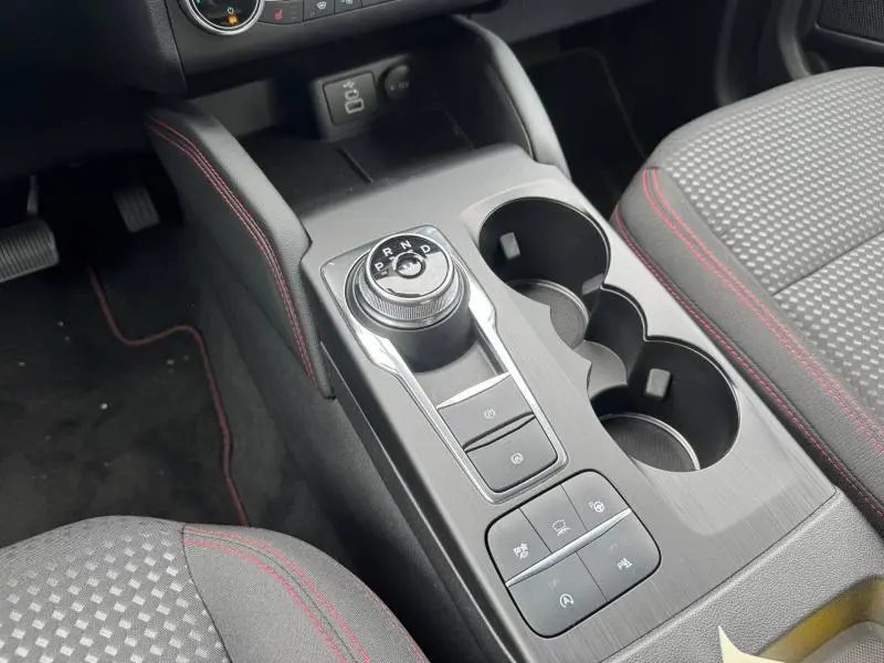 Gros plan sur la console centrale du Ford Kuga gris Solar, avec sélecteur de boîte auto rotatif et porte-gobelets.