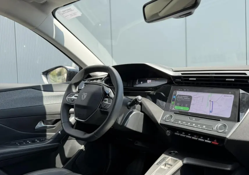 Vue intérieure côté conducteur du Peugeot 308 2025 gris Artense, avec volant cuir et écran tactile central affichant la navigation.