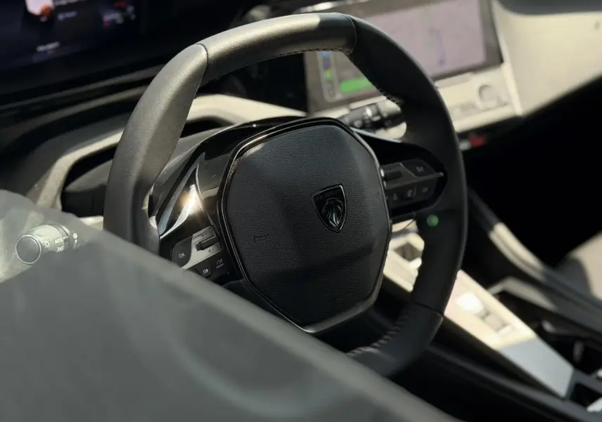 Gros plan sur le volant cuir noir du Peugeot 308 2025 avec tableau de bord numérique et écran tactile en arrière-plan.
