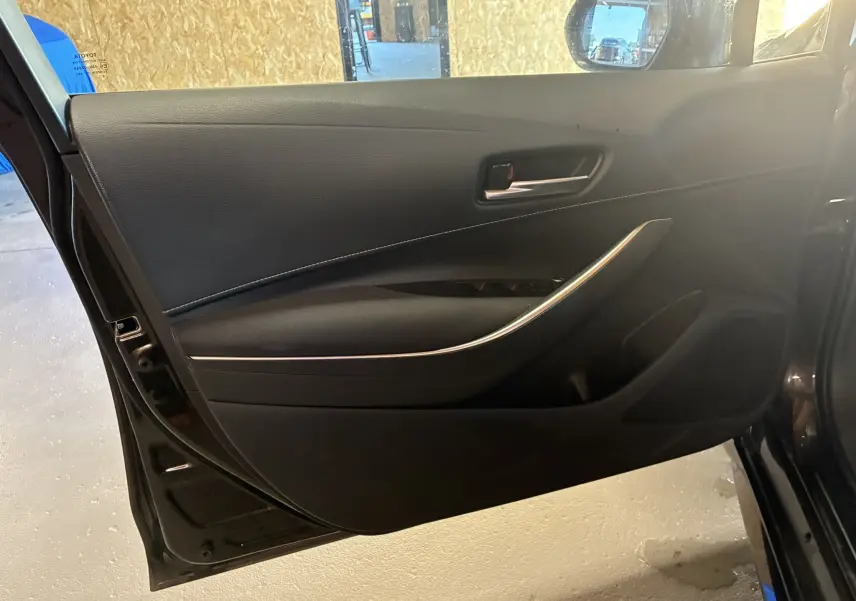 Vue intérieure de la porte avant gauche noire d'une Toyota Corolla 1.8 122 Dynamic avec garniture et poignée chromée.
