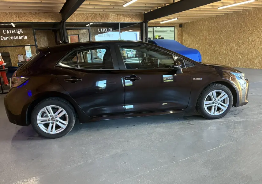 Profil côté gauche d'une Toyota Corolla 1.8 122 Dynamic noire, hybride essence, avec jantes alu dans un atelier.