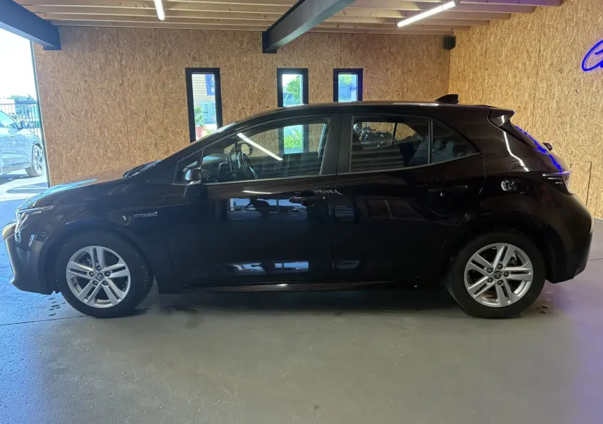 Profil côté gauche de la Toyota Corolla 1.8 122 Dynamic noire, hybride essence, avec jantes alu et rétroviseurs électriques.