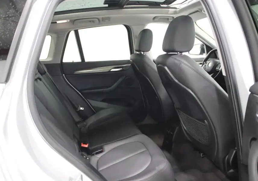 Vue intérieure côté gauche arrière du BMW X1 argenté, mettant en valeur les sièges en cuir noir et le toit ouvrant.