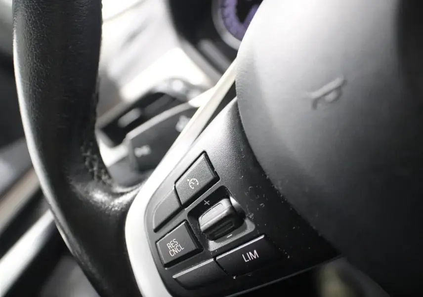 Gros plan sur les commandes de régulateur de vitesse au volant cuir noir du BMW X1 argenté, version sDRIVE 18D BVA X-LINE.