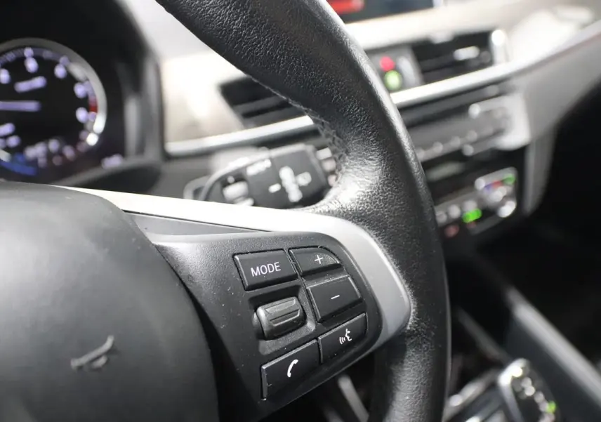 Gros plan sur le volant noir avec commandes multifonctions du BMW X1 sDRIVE 18D 2019, intérieur moderne et lumineux.