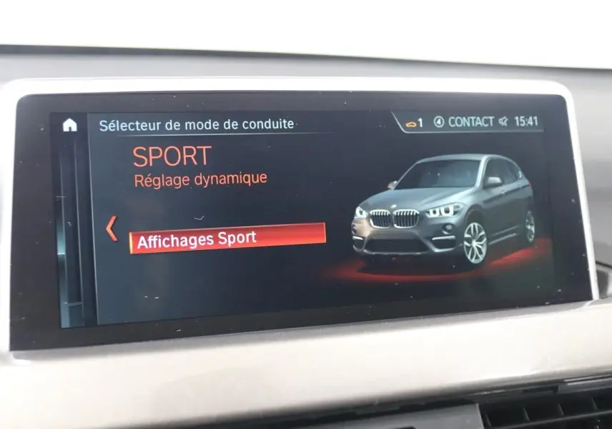Écran de bord affichant le mode de conduite Sport avec une illustration 3/4 avant d’un BMW X1 argent métallisé.
