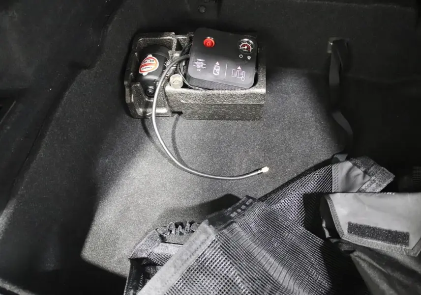 Gros plan sur le coffre d’un BMW X1 argenté, montrant un compresseur d’air intégré et un filet de rangement noir.