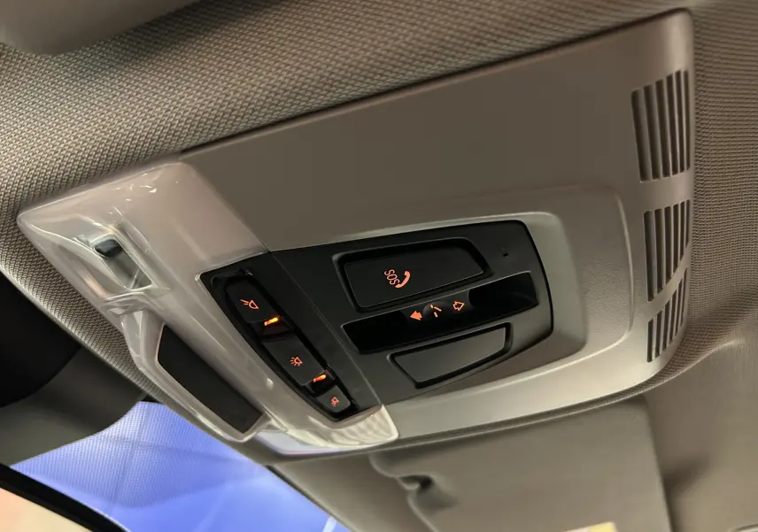 Vue en gros plan du panneau de commandes au plafond avec éclairage orange dans l’habitacle gris clair d’une BMW X1 argent métallisé.