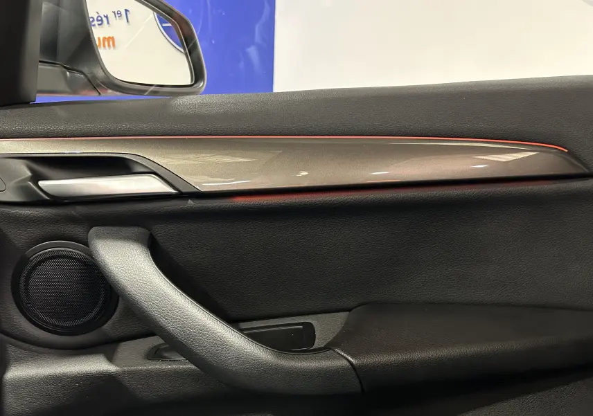 Détail de la porte intérieure côté conducteur d’un BMW X1 argent métallique, avec bande décorative et haut-parleur intégré.