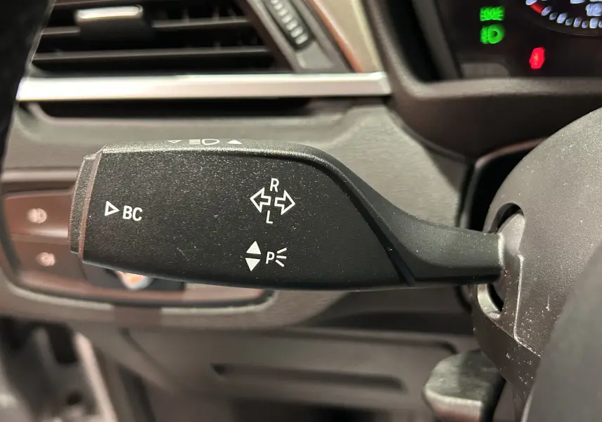 Gros plan sur la manette de clignotant noire à gauche du volant dans l'habitacle d'un BMW X1 argenté de 2019.