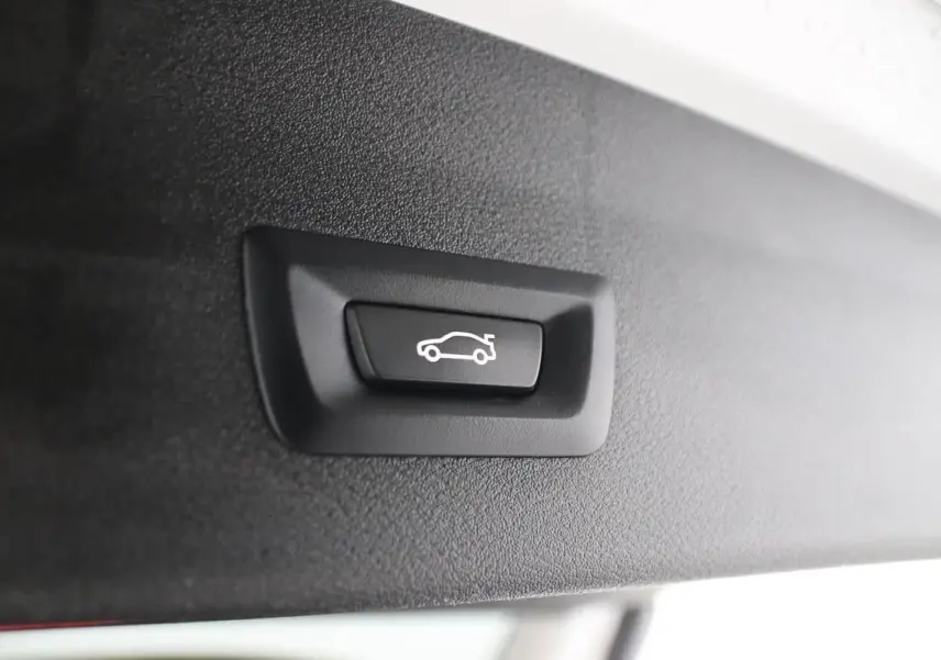 Bouton de fermeture électrique du hayon sur le bord intérieur du coffre d'un BMW X1 argent métallisé.