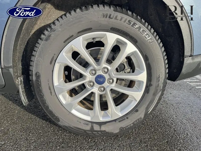 Gros plan sur la roue avant droite du Ford Kuga bleu azur métallisé avec jante alu et pneu Multiseason.