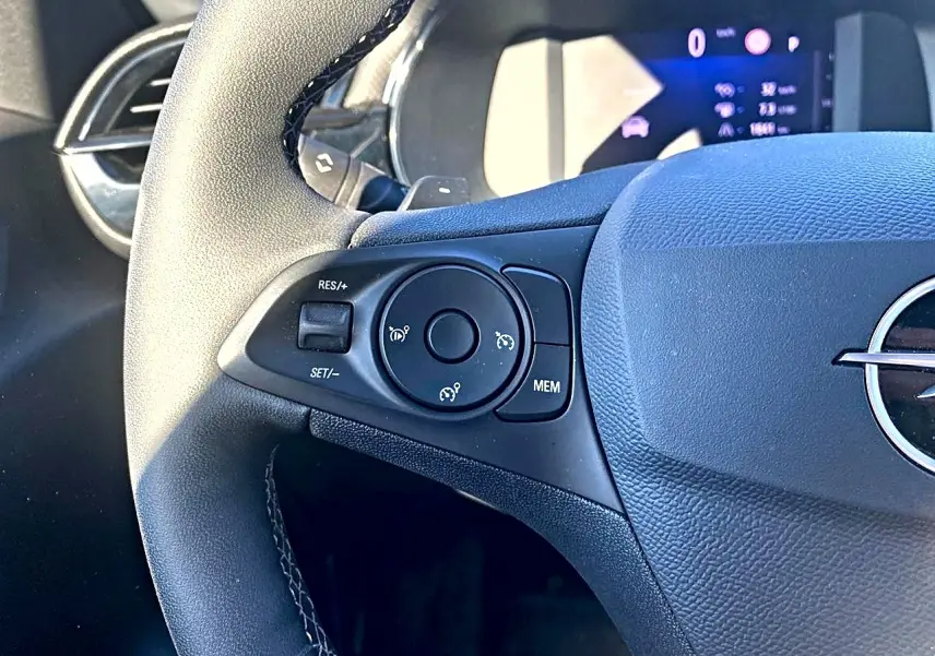 Gros plan sur le côté gauche du volant noir de l'Opel Corsa 2025 avec commandes de régulateur de vitesse et tableau de bord numérique.