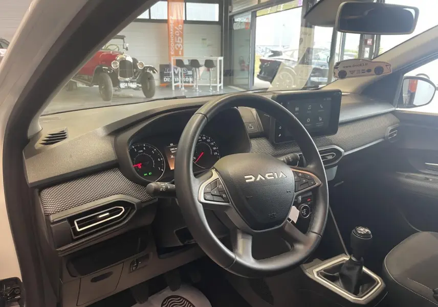 Vue intérieure côté conducteur de la Dacia Sandero blanche 2024, volant multifonction et tableau de bord moderne.