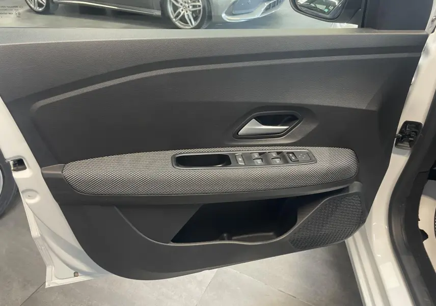 Vue intérieure côté gauche de la porte avant blanche d'une Dacia Sandero 2024 avec commandes de vitres et poignée grise.