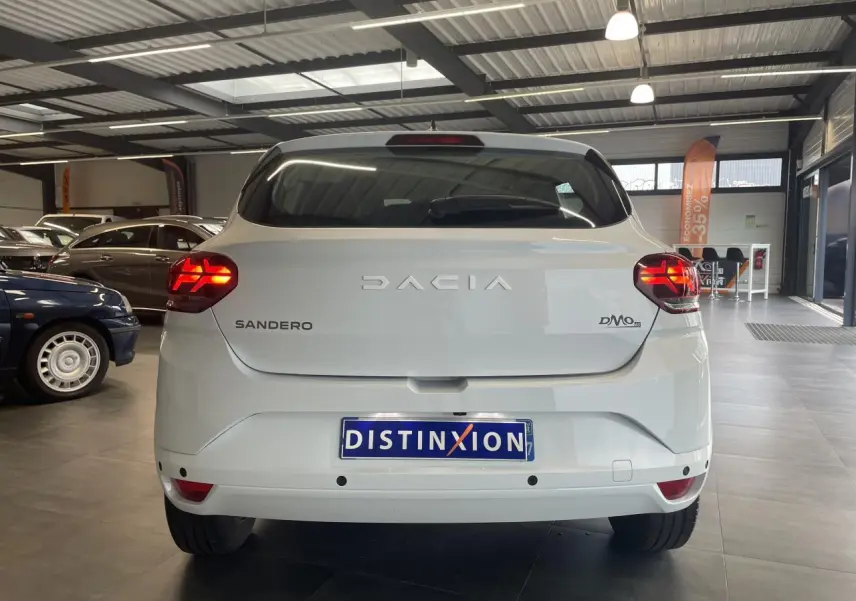Vue arrière d'une Dacia Sandero blanche 2024 avec feux LED allumés dans un showroom.