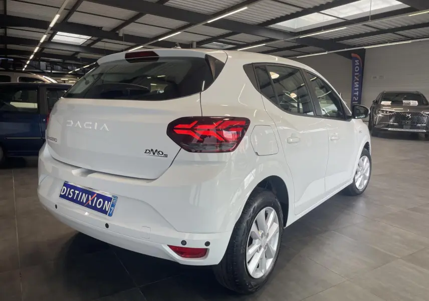 Vue 3/4 arrière droite d'une Dacia Sandero blanche 2024 avec feux LED et enjoliveurs Sorane en showroom.