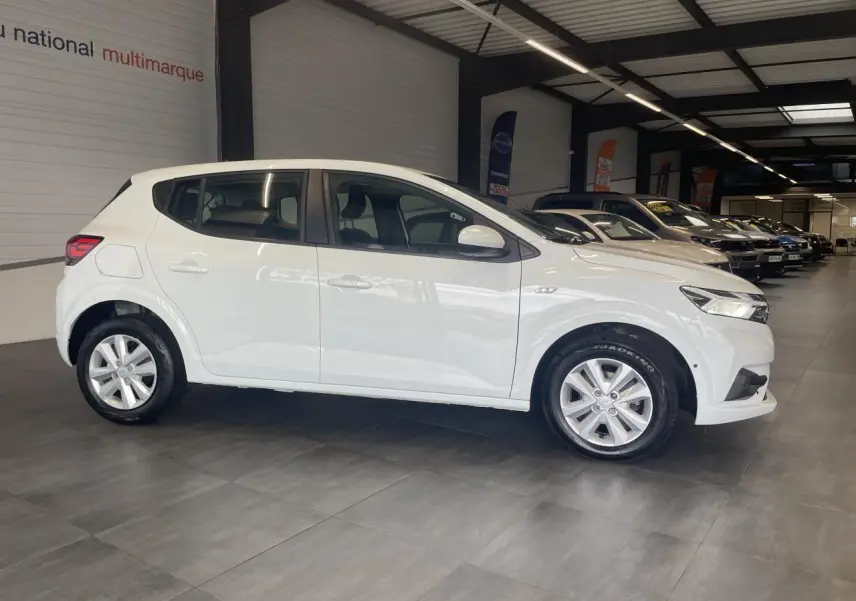 Profil côté gauche d'une Dacia Sandero blanche 2024 en showroom, avec jantes alliage et rétroviseurs couleur carrosserie.