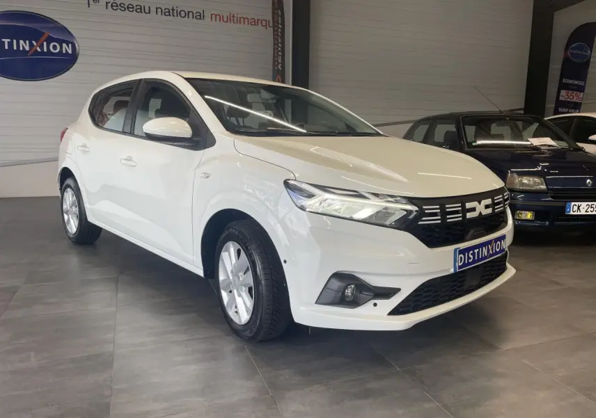 Vue 3/4 avant d'une Dacia Sandero blanche 2024 avec calandre noire et jantes à enjoliveurs.
