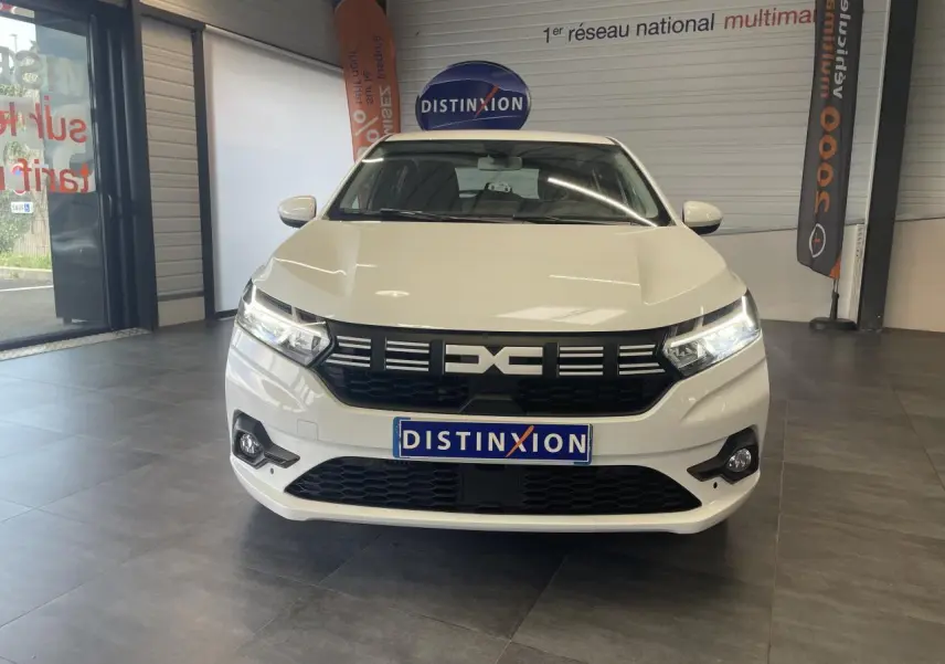 Vue avant d'une Dacia Sandero blanche 2024 en showroom, avec calandre noire et feux LED allumés.