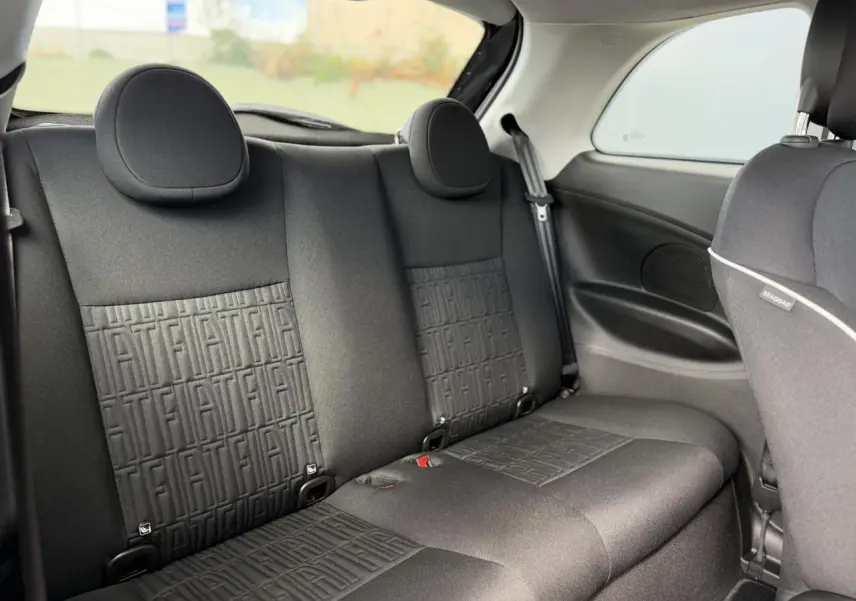 Vue intérieure arrière de la Fiat 500 électrique 2024, montrant la banquette noire avec motifs FIAT embossés.