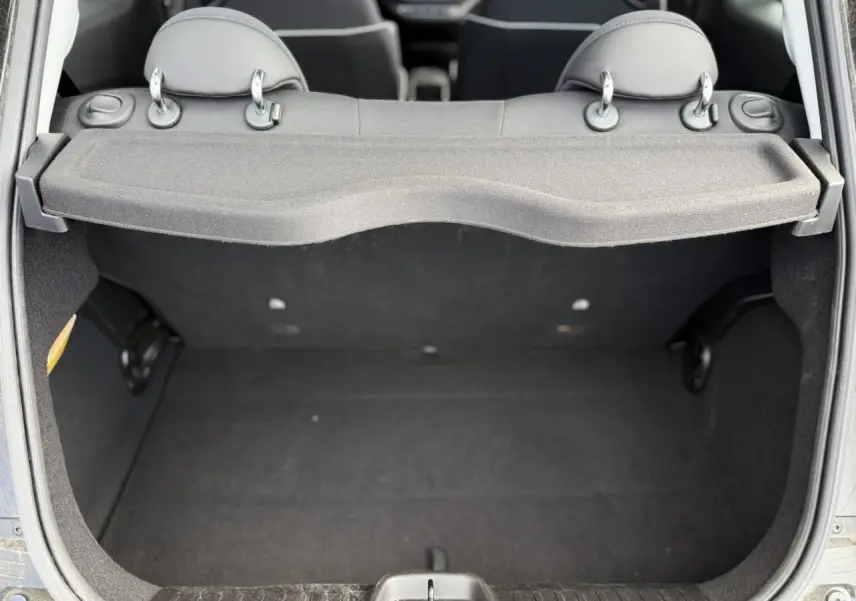Coffre ouvert vu de l'arrière d'une Fiat 500 électrique blanche, montrant l'espace de chargement et les appuie-têtes arrière.