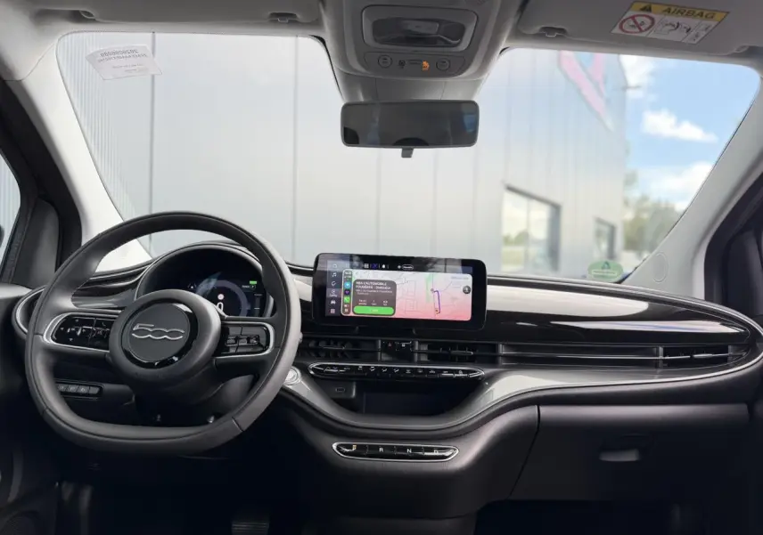 Vue intérieure frontale du tableau de bord noir brillant et volant FIAT 500 électrique avec écran tactile central affichant la navigation.