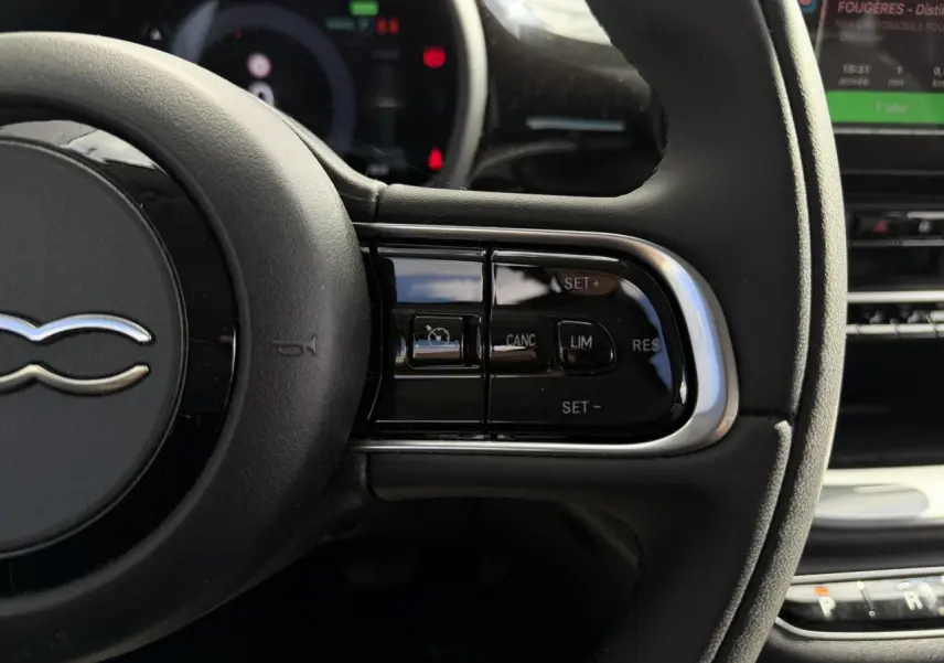 Gros plan sur le volant noir Soft-Touch du Fiat 500 électrique 2024, avec commandes intégrées au côté droit.