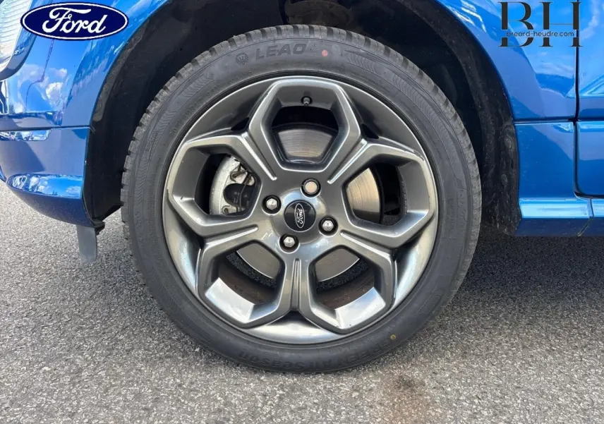 Gros plan sur la roue avant gauche avec jante alu grise du Ford Ecosport bleu Lightning, partie basse de la carrosserie visible.