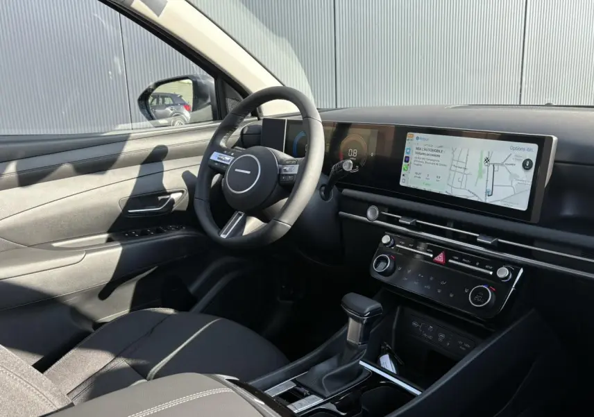 Intérieur avant gauche du Hyundai Tucson 2025 avec tableau de bord numérique et écran tactile large en navigation.