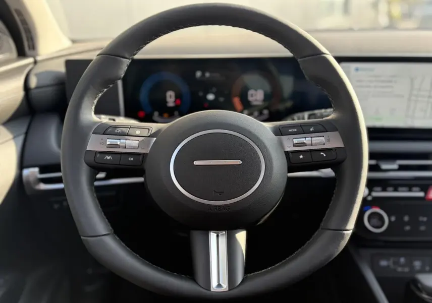 Vue rapprochée du volant cuir noir du Hyundai Tucson 2025, avec tableau de bord numérique et écran tactile en arrière-plan.