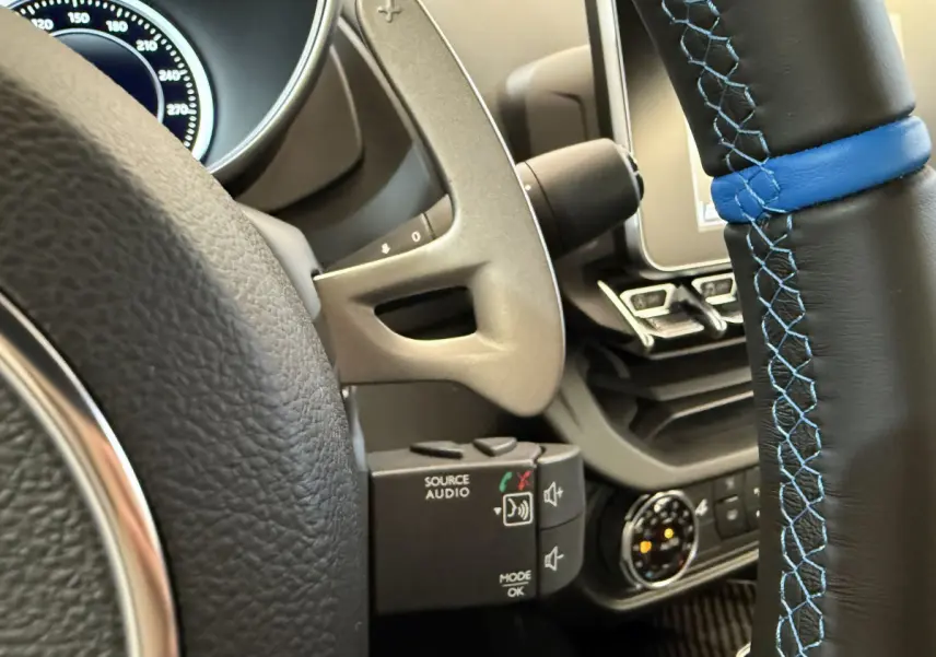 Gros plan sur le volant cuir noir à surpiqûres bleues de l'Alpine A110 Legende 2019 avec tableau de bord et commandes audio.