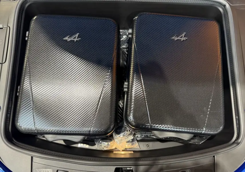 Vue plongeante sur le coffre avant bleu de l'Alpine A110 Legende 2019 avec deux valises noires à motif carbone et logo Alpine.