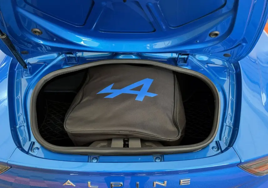 Coffre avant ouvert d'une Alpine A110 Legende bleu 2019, avec sac noir marqué du logo Alpine bleu visible.
