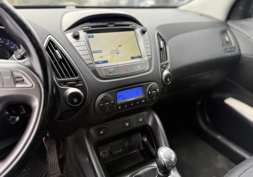 Vue intérieure du tableau de bord du Hyundai ix35 blanc de 2014, avec navigation GPS et levier de vitesses manuel visible.