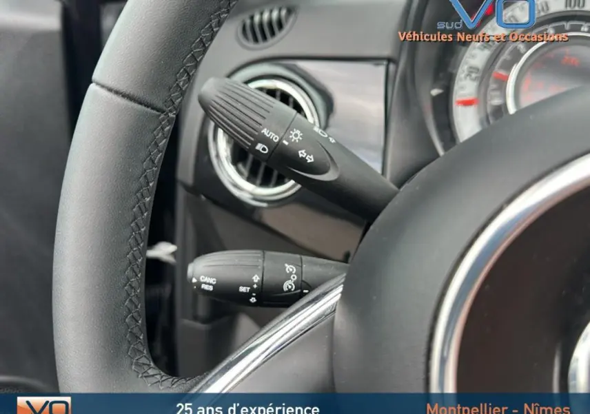 Gros plan sur le volant et les commandes de clignotants d'une FIAT 500C noire, version 2024, intérieur moderne.