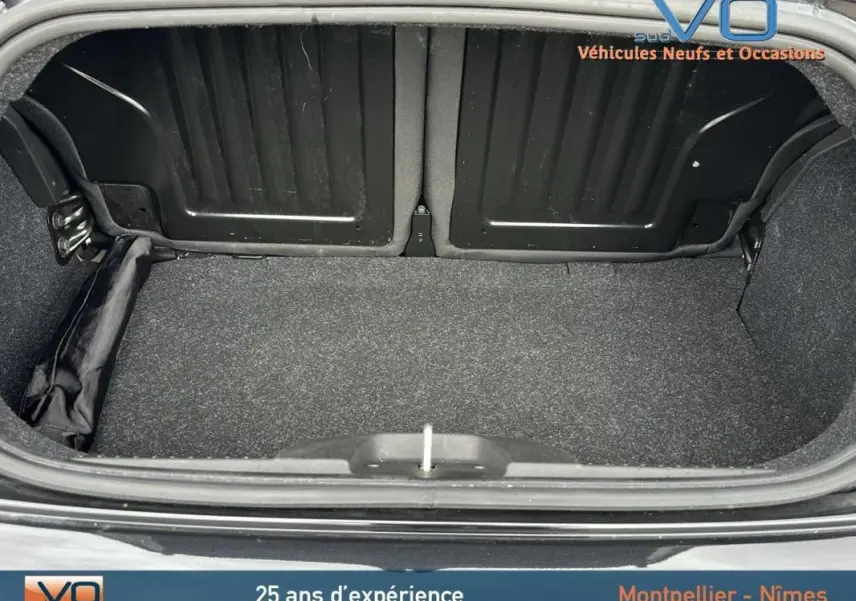 Coffre ouvert vu de l'arrière d'une FIAT 500C noire 2024, mettant en valeur la roue de secours rangée sur le côté.