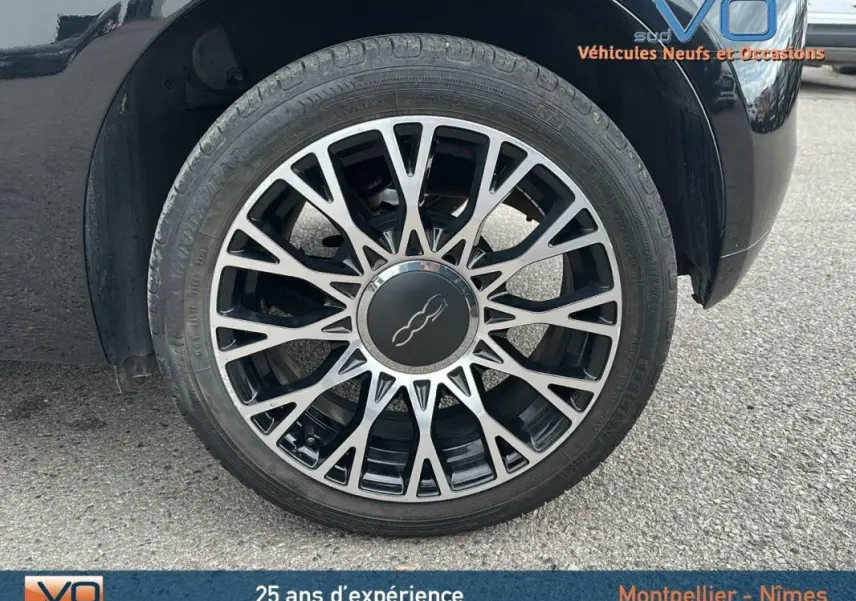 Gros plan sur la roue avant droite noire de la FIAT 500C 2024 avec jante alliage au design complexe et logo central.