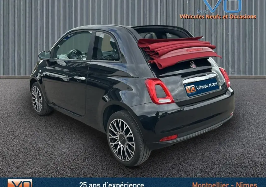 Vue 3/4 arrière droite d'une FIAT 500C noire 2024 avec toit rouge replié et jantes alliage, stationnée sur sol gris.