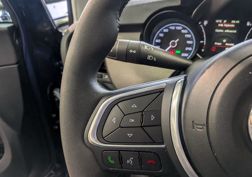 Gros plan sur le volant noir de la FIAT 500X 2024, montrant les commandes multifonctions et le tableau de bord partiel.