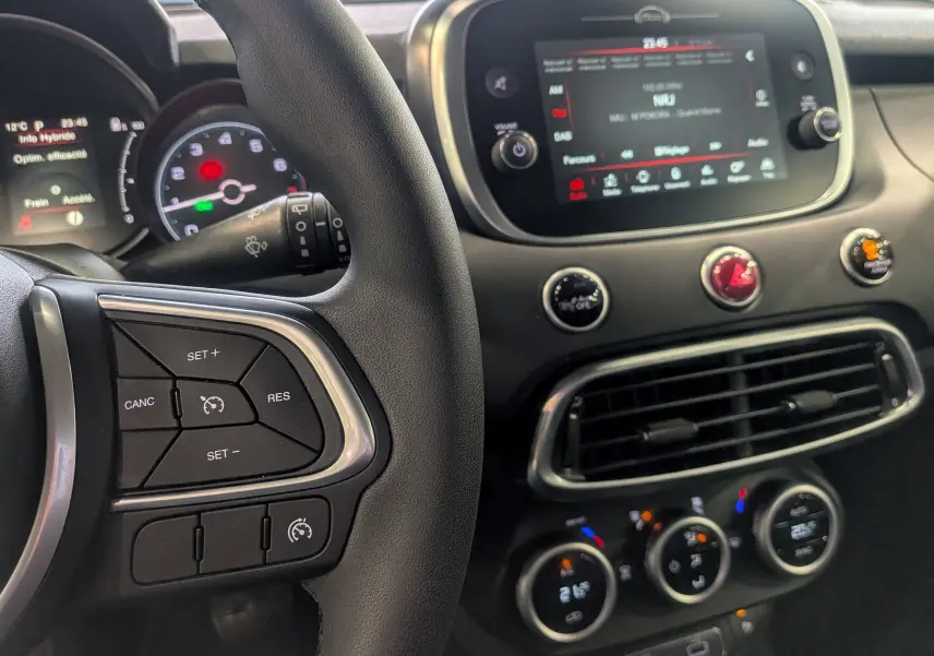 Vue rapprochée de l’intérieur du Fiat 500X bleu Venezia, montrant le volant, l’écran tactile et les commandes de climatisation.
