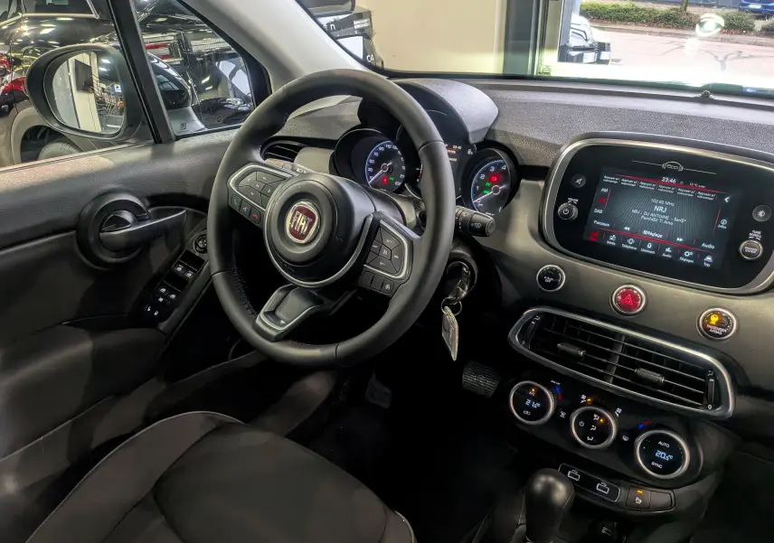 Vue intérieure côté conducteur du Fiat 500X 2024, mettant en valeur le volant multifonction, l'écran tactile et les commandes du tableau de bord.