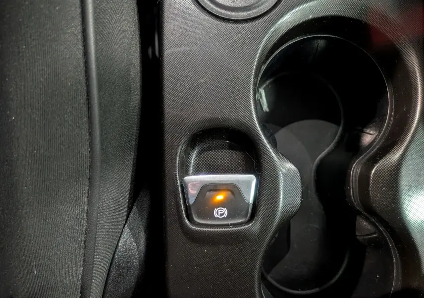 Gros plan sur le bouton de frein à main électrique allumé dans la console centrale d’une FIAT 500X Bleu Venezia 2024.