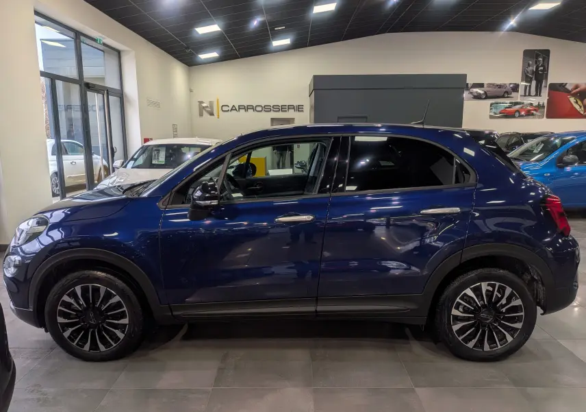Vue de profil côté gauche d'un FIAT 500X bleu Venezia 2024 en hybride essence, avec jantes noires et chromées.