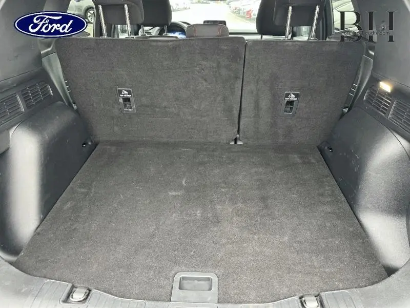 Vue du coffre arrière ouvert du Ford Kuga 2023 gris Magnetic, montrant la banquette arrière en position verticale.