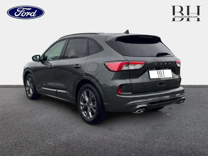 Vue 3/4 arrière droite d'un Ford Kuga 2023 gris Magnetic métallisé avec vitres arrière surteintées et double sortie d'échappement.
