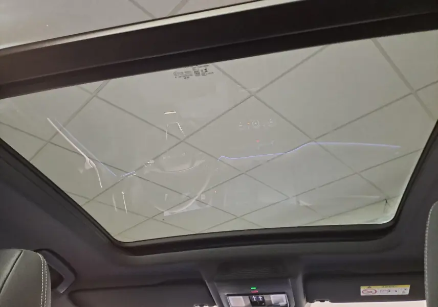 Toit panoramique en verre du Skoda Kodiaq Bleu RS vu de l'intérieur, avec éclairage d'ambiance et ciel reflété.